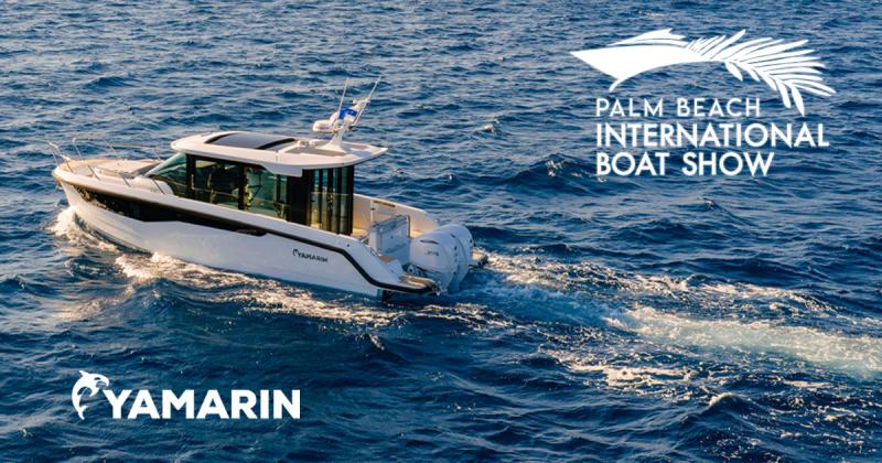 An aerial view of a white Yamarin Aura Cabin motorboat cruising through deep blue ocean water, leaving a white wake behind. The boat features twin outboard engines and a sleek cabin design. The Yamarin logo is in the bottom-left corner, and the Palm Beach International Boat Show logo is in the top-right.